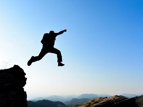 A silhouetted figure jumps off of a rock